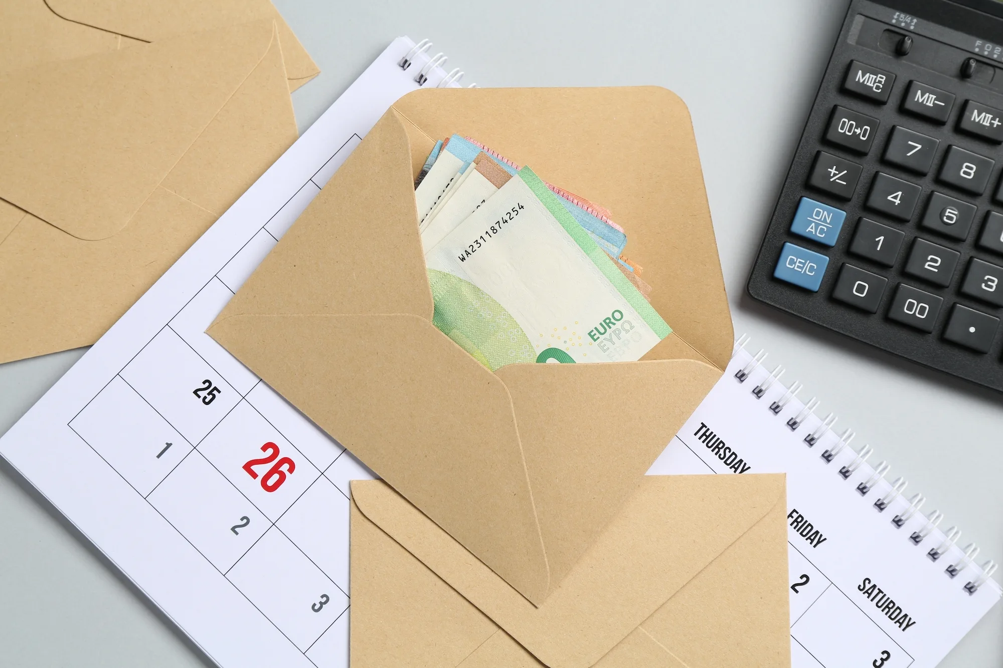 Varios sobres de papel etiquetados con categorías del hogar, dinero dentro y una libreta de apuntes al lado.