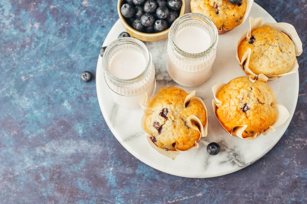 Muffins nutritivos con yogur griego MÍO, dorados y esponjosos, servidos en un plato junto a frutas frescas y un vaso de leche.